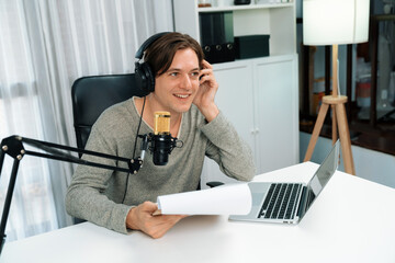 Host channel in smart broadcaster with talking show on live social media streaming with script note reading to listeners, wearing headphones to record video streamer at modern home studio. Pecuniary.