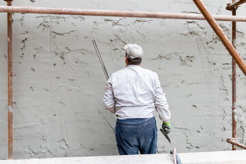 A worker hand removes excess plaster with leveler and spatula. Renovation