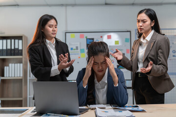 Stressed asian businesswomen argue in office, one with headache, showing pressure of corporate world. Feelings of frustration, anger, sadness evident. Woman looks tired, exhausted, worried