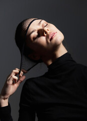 Elegant woman in black attire with a fishnet headpiece, expressing tranquility and confidence against a dark, solid background. Fashion and beauty concept.