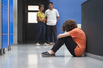 Sad teenager sitting alone on floor victim of bullying. Bullied student crying and suffering...