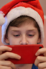 Close-up of the eyes of a teenager wearing a Santa Claus hat looking at a smartphone