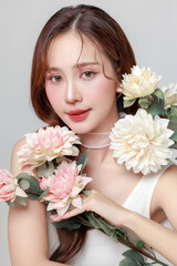 Pretty Asian woman model perfect clear fresh skin smile with flowers on isolated grey background. Portrait female beauty blogger make up artist in studio. Skincare, plastic surgery, spa concept.