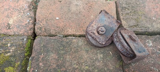 Rusty Metal Pulleys on Moss-Covered Brick Surface. Close-up photo of two aged, rusty pulleys resting on weathered bricks with moss growth, evoking a vintage and industrial atmosphere