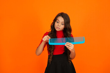 Girl with hairbrush isolated orange. Teen beauty hairstyle. Haircare and hair loss. Shocked girl use hair comb. Comb and hairbrush. Teen girl combing curly hair. Hairdresser. Hair loss. Healthy hair
