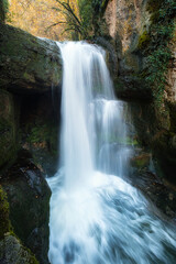Waterfall at Moulin du Saut, an 18th century derelict mill in a forest of autumn colours on the Alzou river in the Lot region of France