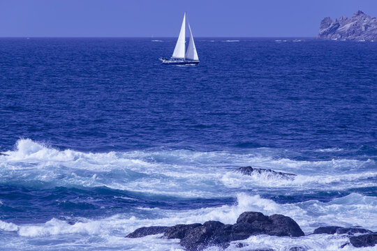 Sailboat Navigating the Blue Waters off the Rocky Coast of Muxia, Galicia, Spain
