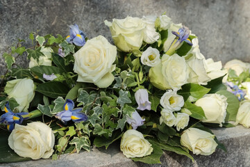 Funeral flowers at the cemetery. Memorial flowers, the main colors are white and blue. A beautiful arrangement of white roses, white eustoma and blue irises and bellflowers.