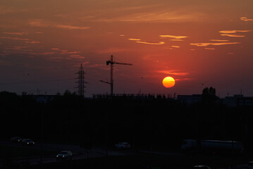 Sunset in Timisoara, Romania with cran cranes and electricity pylons with the sun and a bright red and orange sky