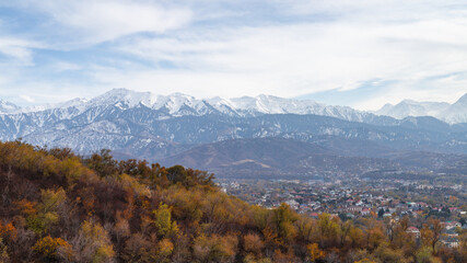 Village in valley with snow-capped mountains, autumn trees, and serene atmosphere.