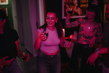 Group of young friends enjoying a vibrant birthday party indoors, laughing and holding drinks. The festive atmosphere and colorful lighting enhance the joyful celebration.