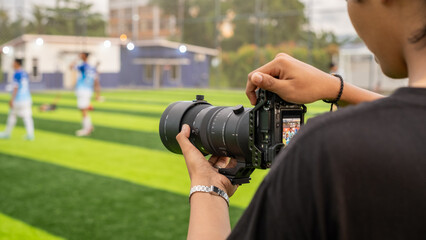 A photographer documenting a mini soccer game using a telephoto lens, focusing on players on a well-maintained green field under natural light, capturing dynamic sports moments