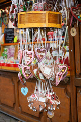 Heart-shaped gingerbread cookies with colorful icing and inscriptions hang from a wooden display at a festive market