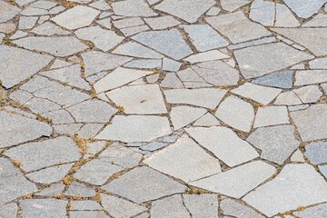 Close-up image of weathered, irregular stone tiles arranged in a herringbone pattern on a paved surface Muted earthy tones dominate the scene with some worn areas revealing underlying dirt or smalle