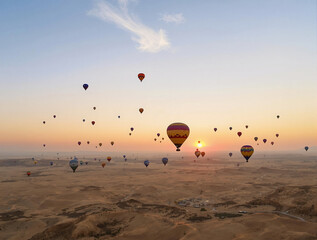 Obraz premium A wide-angle aerial view of colorful hot air balloons floating over a vast desert at sunrise