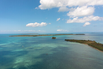 Small islands surrounded by coral reefs and blue sea in Bantayan, Cebu. Blue sky and clouds. Boat running on water. Philippines.