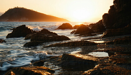Obraz premium A rocky beach at golden hour, with the sun low in the sky casting a warm, orange glow over the scene