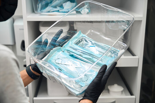 Man dentist holding plastic container with closed packages with sterile dental tools