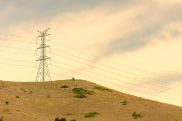 Photograph of a large electricity Transmission Tower on a grassy hill against an orange sunset sky in regional Australia.