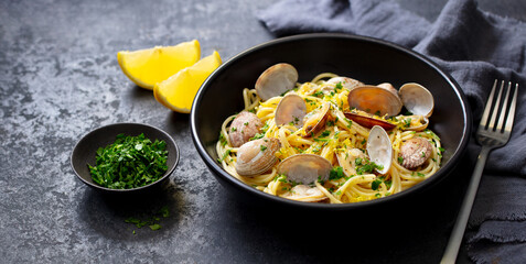 Spaghetti with clams, seafood pasta alle vongole in a black bowl. Dark background. Close up.