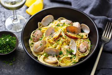 Spaghetti alle vongole, seafood pasta with clams in a black bowl and glass of wine. Dark background. Close up.