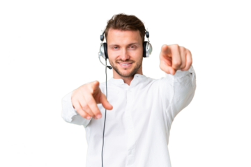 Telemarketer caucasian man working with a headset over isolated chroma key background points finger at you while smiling