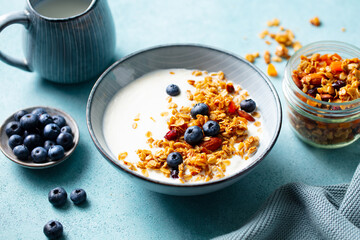 Oat granola with fresh blueberries and milk in a bowl. Blue background. Close up.