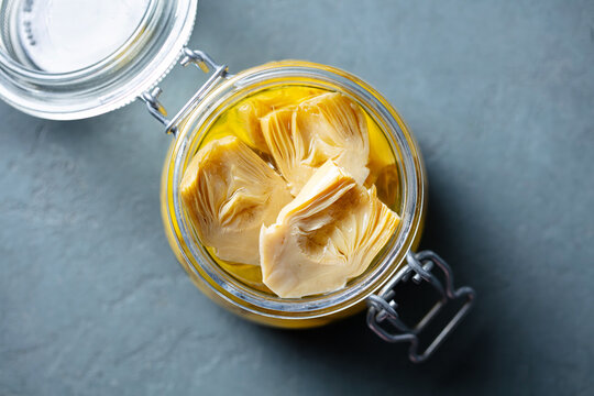 Artichoke hearts marinated in olive oil in glass jar. Close up. Top view.