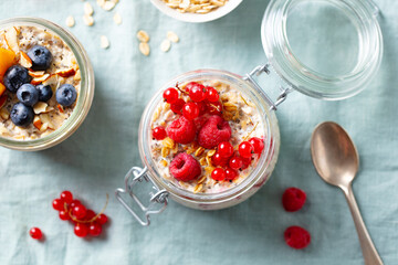 Overnight oats with fresh berries and fruits in glass jars. Blue textile background. Close up. Top view.