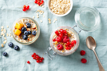 Overnight oats with fresh berries and fruits in glass jars. Blue textile background. Top view.