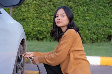Young Asian woman smiling, carefree, inflating a car tire, tire inflating service at a gas station Check car wheel air pressure and maintain car wheel safety. Safe driving concept.