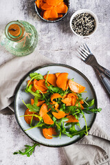 Vegetarian salad with sweet potato and arugula on a plate on the table top and vertical view