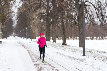 Winter running in park: happy woman runner jogging in snow, outdoor sport and fitness concept 