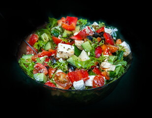 Greek Salad salad bowl made of dark glass close-up on a dark background