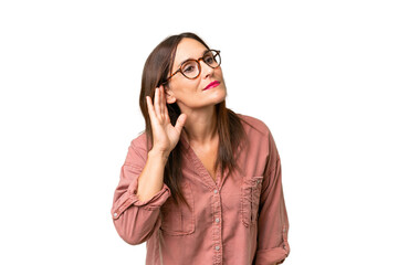 Middle-aged caucasian woman over isolated background listening to something by putting hand on the ear