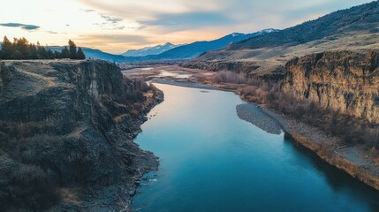 Obraz premium Serene river flowing through a valley at sunset, mountains in the background.