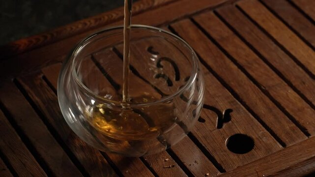 Tea ceremony on dark background. Pouring red/black tea in cup. 