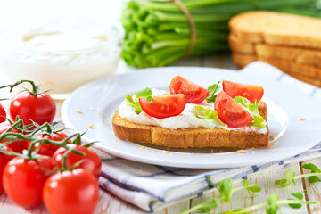 Toasted bread with cream cheese and cherry tomatoes on the dinner table. A light appetizer for a party or picnic.