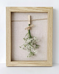 Small dried flowers tied with twine displayed in a wooden frame over textured canvas