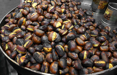 Roasted chestnuts cooked in a large metal pan for sale at a street food stall