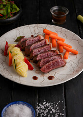 Grilled beef steaks and vegetables, With cooked carrots and mashed potatoes, black wood background