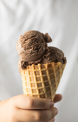 a human hand holds a ice cream cone up. nine year boy eating ice cream on white