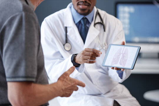 Cropped shot of doctor wearing lab coat holding tablet with lung diagram while explaining diagnosis and treatment to senior patient during consultation in clinic, copy space
