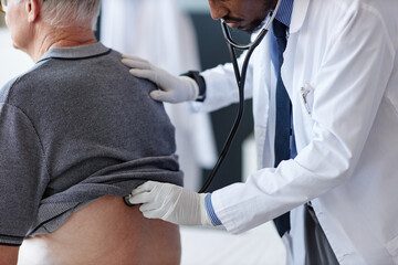 Side view close up of African American doctor using stethoscope while carefully examining back of...