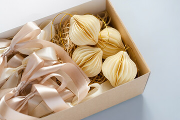 Craft box with satin bows in pastel colors and beige paper ornaments for decorating a Christmas tree on a light blue background. Festive mood and decorating a Christmas tree concept