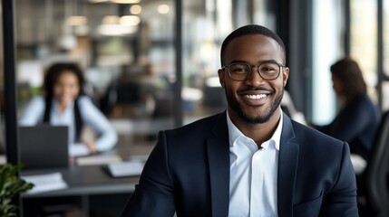 Professional in modern office environment displaying genuine warmth with bright smile, wearing smart business attire and glasses against blurred workspace background with colleagues.