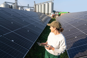 Female farmer with digital tablet on a modern farm using solar panels. Agricultural silos in the...