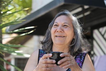 senior latin woman drinking coffee or tea outdoors on sunny summer day  