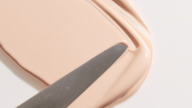 Smear foundation face make-up cream or beige concealer smudge with cosmetic spatula. Beauty texture background.