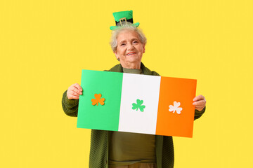 Happy senior woman with leprechaun hat and Irish flag on yellow background. St. Patrick's Day...